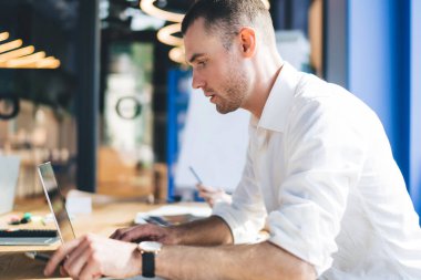 Bilgisayarı kullanırken ve konsantrasyonla istatistik çalışırken çağdaş ofiste masada oturan zeki bir adamın yan görünümü