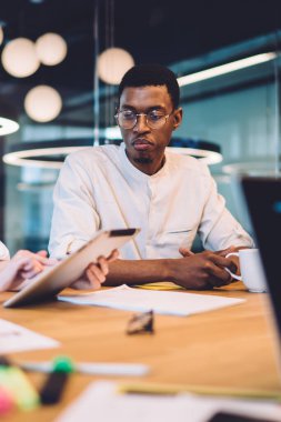Modern konferans odasındaki ahşap masada otururken laptopta çalışan ve sabah kahvesi içen çok ırklı meslektaşlar.