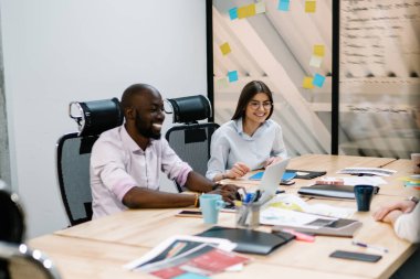 Masada oturan çok ırklı beyaz gömlekler dizüstü bilgisayarlarla dolu. Ofisteki tablonun karşısındaki kahve fincanlarıyla dolu.