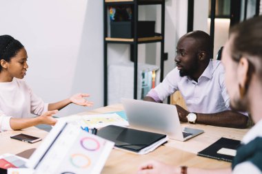 Gündüz vakti iyi aydınlatılmış brifing ofisinde iş stratejisi tartışmasına katılan çok ırklı genç meslektaşlardan oluşan bir ekip.
