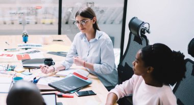 Yukarıdan gelen çok ırklı hedef odaklı iş arkadaşları başlangıç geliştirmesini tartışıyor ve modern çalışma alanındaki kırtasiyeli dağınık masa etrafında iş çözümleri arıyorlar.