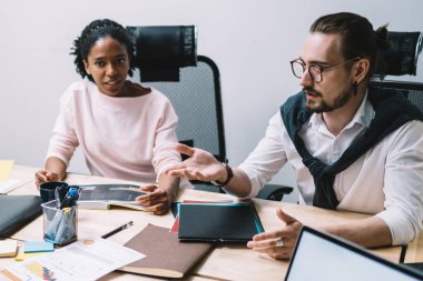 Resmi olarak dalgın girişimcinin yüksek açısı, açık modern ofis toplantılarında kağıt ve dizüstü bilgisayarla ahşap masada otururken dalgın meslektaşlarına bakış açısını açıklıyor.