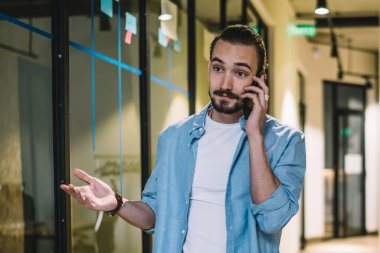 İş konularını telefonda tartışan, ofis binasının koridorunda dururken el kol hareketi yapan, gündelik giysiler içinde, anlaşılmaz genç bir erkek.