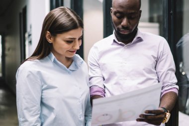 İş yerinde gülümseyen genç bir bayanın çizelgesini göstermesiyle başlayan, günlük kıyafetleriyle başarılı Afrikalı erkek.