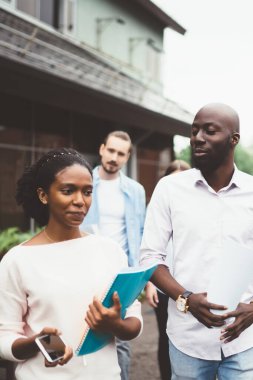 Şehir ve fabrika borularının arka planına karşı bina yakınlarında yürürken insanlar işi tartışıyor ve belgeleri ellerinde tutuyorlar.