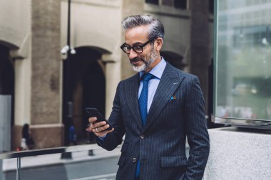 Orta yaşlı resmi takım elbiseli, New York 'ta şeffaf balkonda el ele duran ve cep telefonu kullanan bir iş adamı.