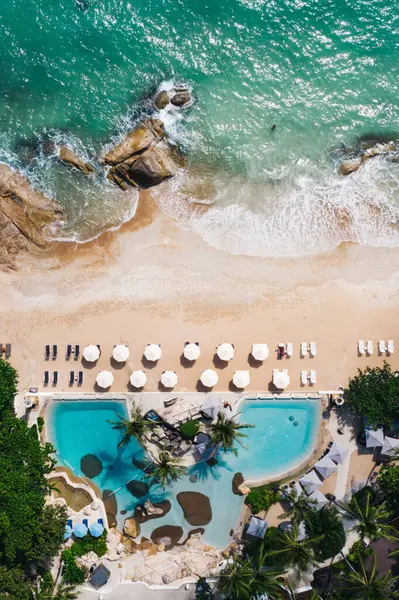 Açık yüzme havuzu ve güneş pansiyonları olan deniz manzaralı otel oteli. Yaz tatilinin kuş bakışı manzarası, turkuaz deniz suyu ve temiz kum kıyısındaki şemsiyeler