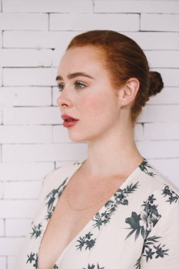 Beyaz tuğla duvarın önünde dikilen güzel, düşünceli, güzel, güzel, kızıl elbiseli kadının yan görüntüsü.