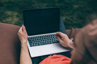 Yukardan bakıldığında sıradan giyinmiş genç bir adamın fasulye torbası üzerinde oturup bilgisayar kullanarak parkta yeni bir proje oluşturduğu görülüyor.