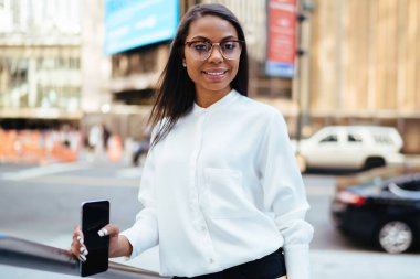 Başarılı koyu tenli ofis çalışanı portresi dijital smartphone aygıt kameraya gülümseyen elinde tutan şık gömlek giymiş. Klasör konumu şehir merkezinde olan mutlu kadın avukat