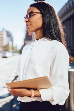 Hukuk Fakültesi holding klasörün şehir kentsel ortamda ayakta eller belgelerle büyüleyici Afro-Amerikan öğrenci yan görünüm. Kentsel ortamda başarılı koyu tenli çalışan durulması