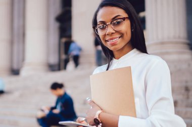 Müreffeh neşeli Afro-Amerikan öğrenci portresi smartphone ağlarda profili güncelleştirilirken kameraya gülümseyen beyaz gömlek giymiş. Pozitif koyu tenli kadın avukat ile ağıl