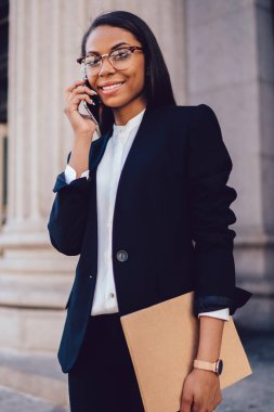 Başarılı kadın memur portresi Smartphone'da iletişim formal giyim giymiş. Telefon ayakta university yakınındaki konuşurken klasörle Hukuk Fakültesi neşeli Afro-Amerikan öğrenci