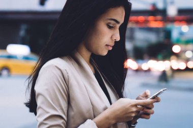 Şehir caddesinde modern binalara karşı duran, resmi kıyafetleri içinde, akıllı telefonları karıştıran konsantre, güzel, modern bir kadın.