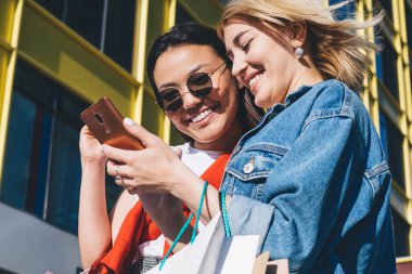 Neşeli bir kadın güneş gözlüklü, alışveriş merkezinin dışındaki akıllı telefon fotoğraflarına bakıyor.