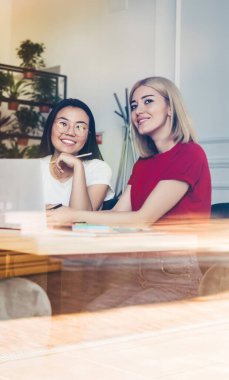 Dizüstü bilgisayarla çalışan ve sanat stüdyosunda raflardaki saksıların karşısındaki masaya oturup notlar alan çeşitli neşeli kadınlar.