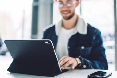 Masadaki siyah kutuda yumuşak odak tableti. Zarif gülümseyen erkek öğrenci masada oturmuş sohbet ediyor.