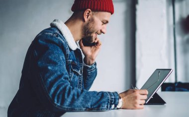 Genç, şık, sakallı, ceketli, kırmızı şapkalı, iş yerinde telefonla konuşan ve ekrana gülümseyen serbest bir genç.