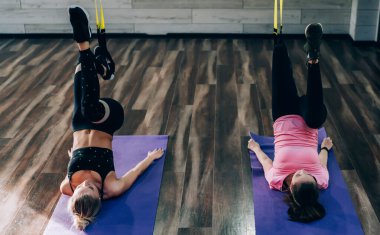 Stüdyodaki fitness sınıfındaki uzaklaştırma eğitimi sırasında mavi spor mindere uzanan ve bacaklarını kaldıran genç kadınların yan görüntüsü.