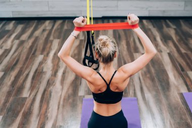 Spor salonundaki spor salonunda lastik bantlı, spor salonu paspası üzerinde oturan sarışın kadın eğitimine yukarıdan bakıyorum.