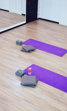Kahverengi lamine zeminde mor yoga minderleri olan ve duvardaki büyük aynaya yansıyan boş spor salonundan.