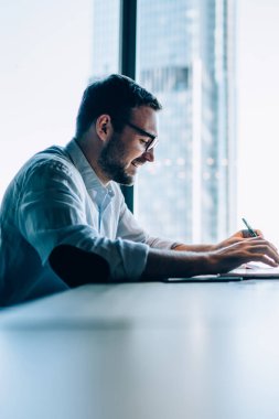 Ofis içi ofis masasında oturan başarılı ofis çalışanının yan görüntüsü. Ticari bilgi aramak için modern ağ kitabı kullanıyor. Kafkas erkek yatırımcı internet sitesini kontrol ediyor.