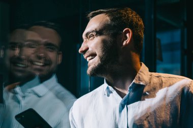 Başarılı genç erkek yönetici cep telefonu teknolojisinde 4G internet kullanıyor ve gülüyor, neşeli Kafkasyalı ofis şirketinde iş günü boyunca akıllı telefon cihazıyla hareketliliğin keyfini çıkarıyor.