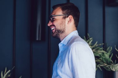 Resmi giysiler içinde neşeli erkek yönetici elinde dizüstü bilgisayarla ve iş arkadaşlarıyla mesajlaşırken kahkahalar atıyor. Modern çalışma ortamında netbook kullanan mutlu patron.