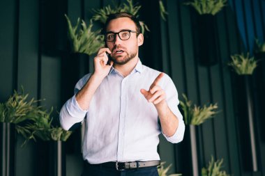 Optik gözlüklü beyaz erkek girişimcinin yarısı kameraya bakarken mobil teknolojiyi şirket bilgilerini tartışmak için kullanıyor. Müşteri hizmetleri üzerinden CEO biletleri ayırtmaktan gurur duyuyor.