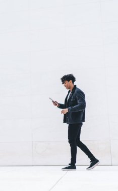 Modern stil gülümseme yan görünümü memnun genç Afrikalı Afrikalı Amerikalı adam günışığında şehir caddesinde yürürken tablet üzerinde gezinen günlük kıyafet