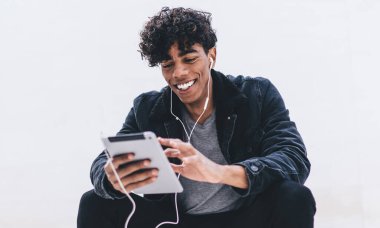 Gülümseyen erkek blogcu internet sitelerinde kulaklıkla komik filmler seyrediyor dokunmatik ped üzerinden hipster adam fotokopi alanına yakın müzik dinliyor ve dijital tabletle son haberleri okuyor.