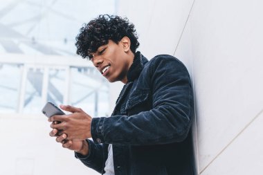 Cep telefonu cihazlı, olumlu gülümseyen adam internet mağazasındaki satışlarla ilgili haberler alıyor. Milenyum hipster 'ı, şehrin arka planında akıllı telefon mesajı ya da yayınını okuyarak ayakta duruyor.