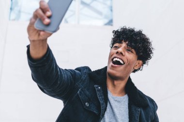 Modern akıllı telefon cihazında selfie çeken komik genç adam, pozitif hipster adam arkadaşlarıyla açık havada iletişim kurmak için 4G kablosuz kullanarak cep telefonuyla konuşuyor.