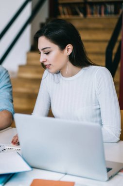 Akıllı erkek ve kadınları heveslendiriyor dikkatle çalışıyor ve kütüphanede dizüstü bilgisayarlı açık kitaplarda bilgi arıyor.