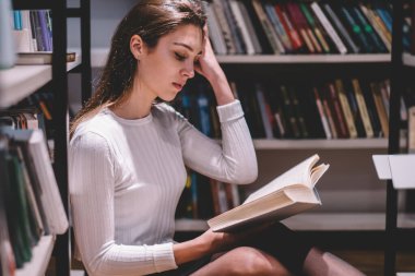 Uzun siyah saçlı, kısa etekli, entellektüel ve zeki bir kadın. Günlük kıyafetleriyle yerde oturmuş kütüphanede kitap okuyor.