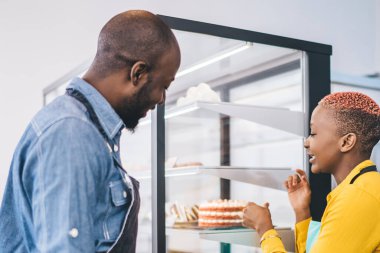 Küçük bir şekerleme dükkanının genç Afrikalı Amerikalı sahiplerinin yan görünüşü pasta vitrinine bakıyor ve yeni bir iş kurarken ürün markasını tartışıyorlar.