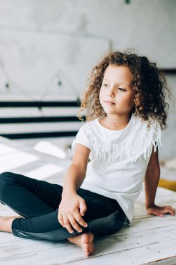 Şaşkın, sevimli, kıvırcık saçlı, günışığında tahta kürsüde bacak bacak üstüne atmış bir çocuk.