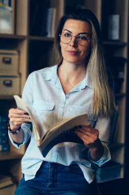Genç büyüleyici pozitif düşünceli kadın kişi uzakta Kitaplığı'nda otururken seyir daha iyi görüş için gözlük. Boş vakit ellerini dergide holding muhteşem hippi kız