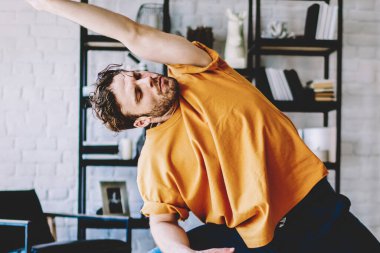 Odaklanmış atletik güçlü erkek turuncu tişörtlü ve mavi pantolonlu. Yoga yapıyor. Beyaz ve siyah halıda.