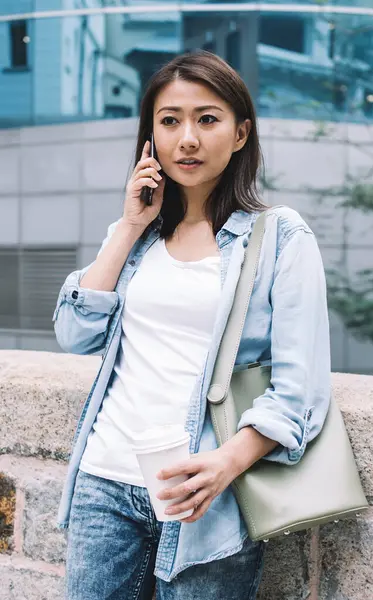 Tuğla çitlere yaslanmış el çantasıyla ve elinde kahve tutarken telefonla konuşan oldukça güzel, etnik bir kadın.