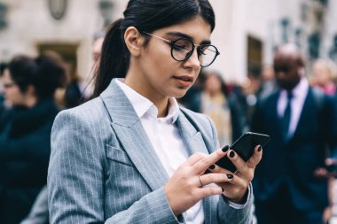Yuvarlak gözlüklü saygıdeğer bayan girişimci elinde çantasıyla karşıdan karşıya geçiyor ve bulanık arka planda sosyal ağda sohbet ediyor.
