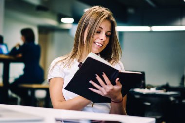 Yapılacaklar listesi öğeleri iade Not defteri planlama, neşeli kız öğrencinin kompozisyon belirterek için yaratıcı fikirler sahip ev ödevi için görevleri tamamlamak ile memnun tutan hippi kız gülümseyerek