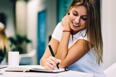 Web sayfasında serbest iş, gülümseyen kız öğrencinin zeki memnun defter incelenmeleri makale yazmaya konsantre neşeli genç kadın kampüs Wi-Fi ve netbook ödev hazırlamak