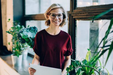 Optik gözlüklü, beyaz kadın serbest portresi. Uzaktan kameraya gülümseyen, modern laptop cihazı üzerinde çalışan, netbook kullanan mutlu kadın.