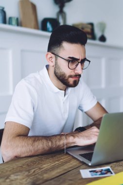 Düşünceli, düşünceli, gözlüklü bir adam dizüstü bilgisayara bakıyor ve daktilo yazarken zeki bir kadın masada el ele oturduğunu düşünüyor.
