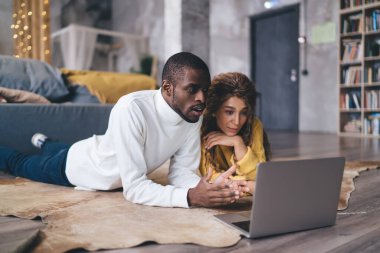 Odaklanmış çift yerde uzanıyor, rahat, şık oturma odalarında dizüstü bilgisayar izliyorlar. Birlikte sessiz ve düşünceli bir anı paylaşıyorlar. Arkadaşlıklarından keyif alıyorlar.