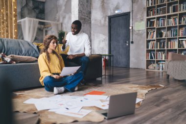 Evrak işleriyle uğraşan odaklanmış bir çift. Belgeleri kasıtlı ifadelerle tartışıyorlar. Konforlu ve modern ortam, takım çalışmalarını ve organizasyon ve planlamaya olan bağlılıklarını vurguluyor.