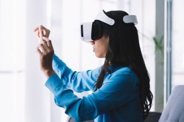 VR cihazını kullanırken ve artırılmış gerçeklikle etkileşime girerken koltukta oturan odaklanmış genç bir kadının yan görüntüsü