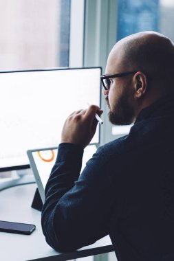 Ofisteki pencereye karşı dizüstü bilgisayar ve tabletle çalışan gözlüklü yetişkin sakallı adamın arka planı