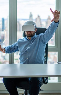Sanal gerçeklik gözlüğü takan profesyonel bir adam ve şehirde bilgisayar masasında otururken yakınlaştıran bir ekran gibi el kol hareketi yapıyor.